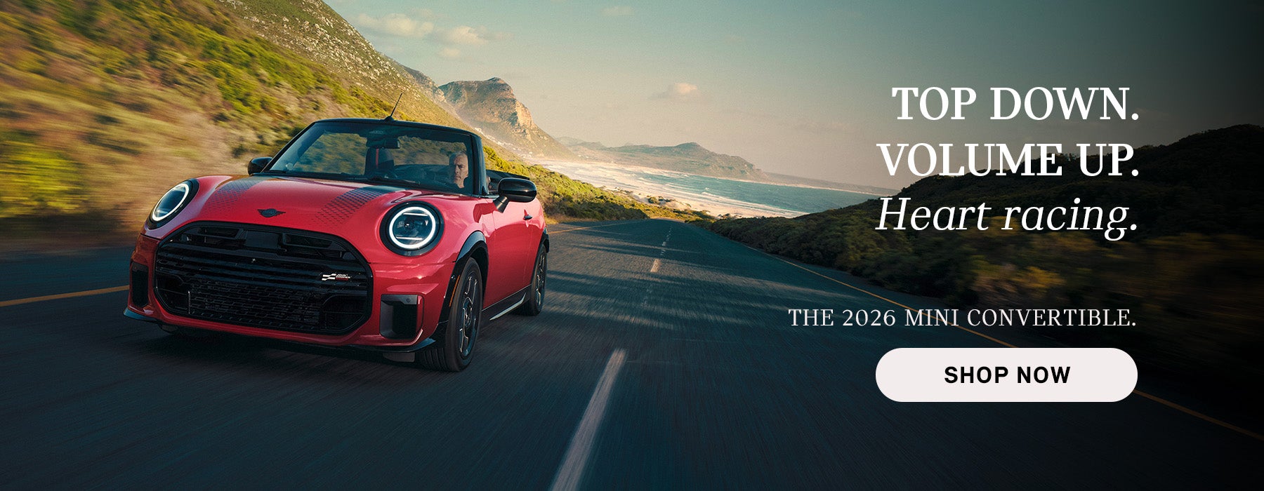 Red MINI convertible driving along a coastal road with mountains and ocean in the background
