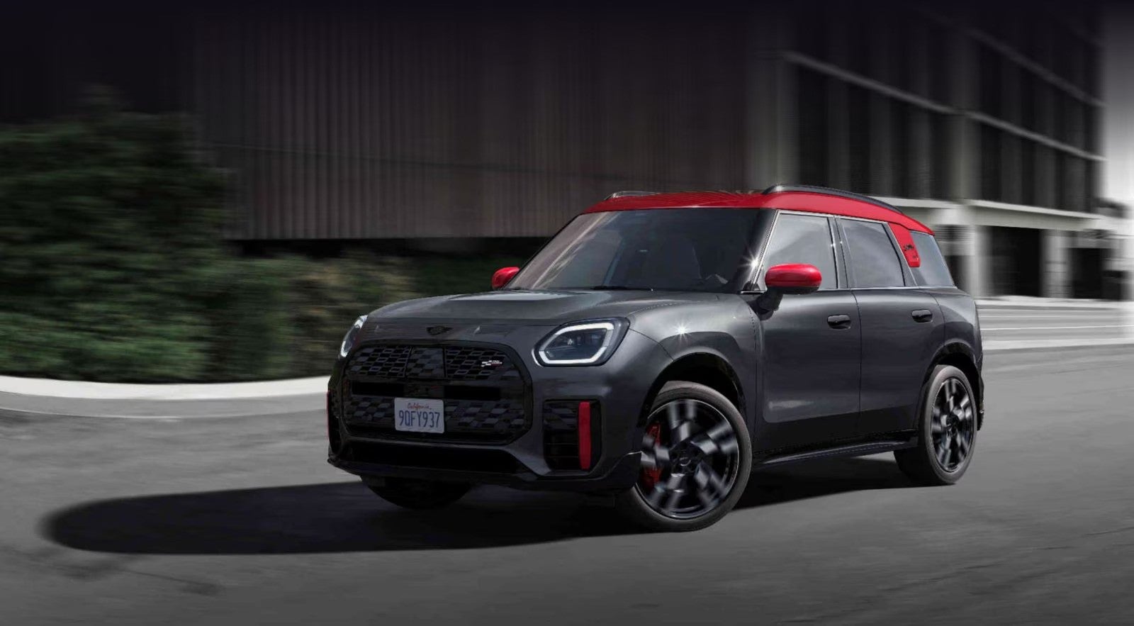  Three-quarters front view of a MINI JCW Countryman ALL4 driving in an urban setting with its shadow underneath it and surroundings blurred out.