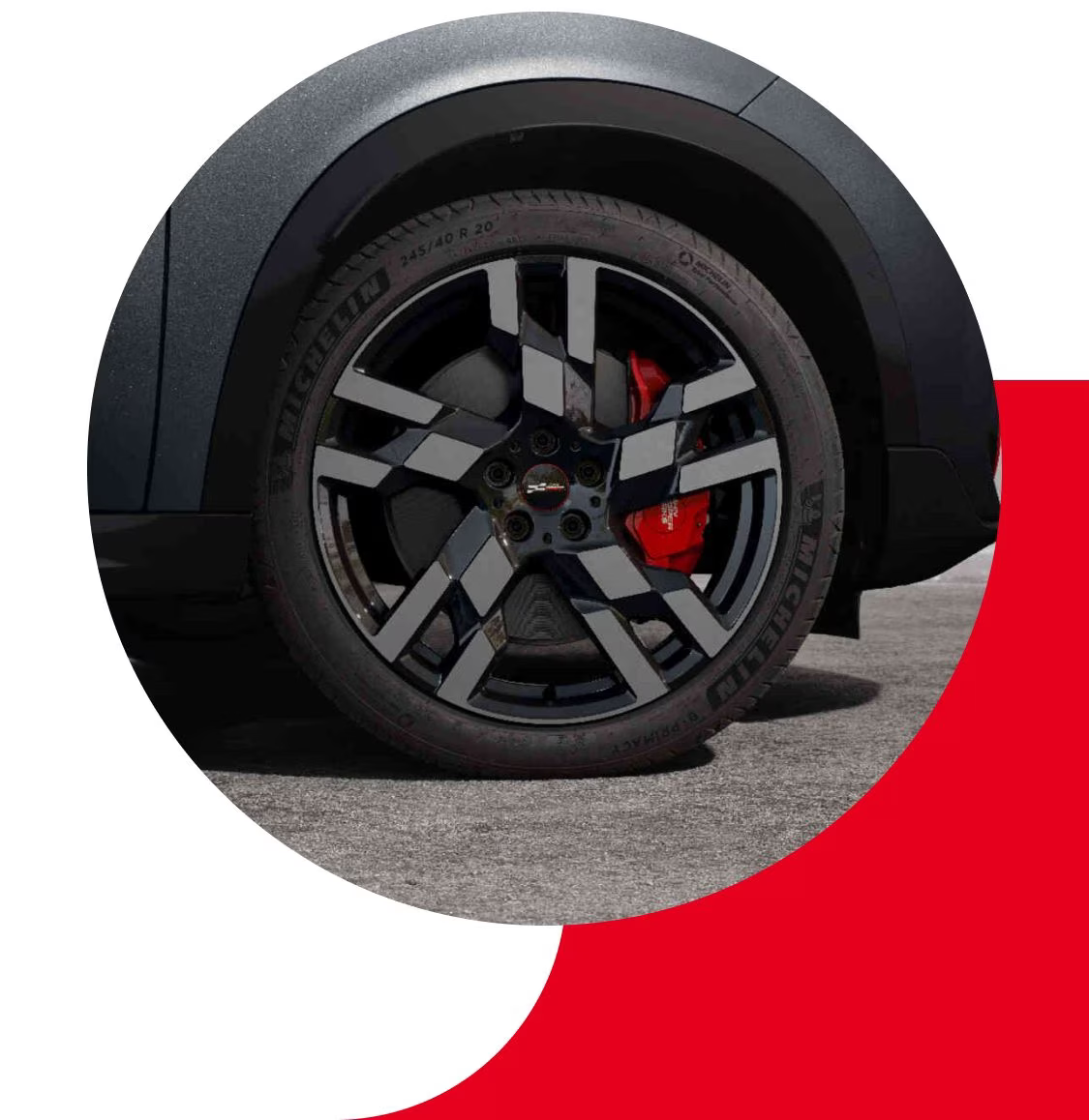 Closeup view of a tire on a MINI JCW Countryman ALL4, parked on a pavement surface with a shadow underneath the vehicle.