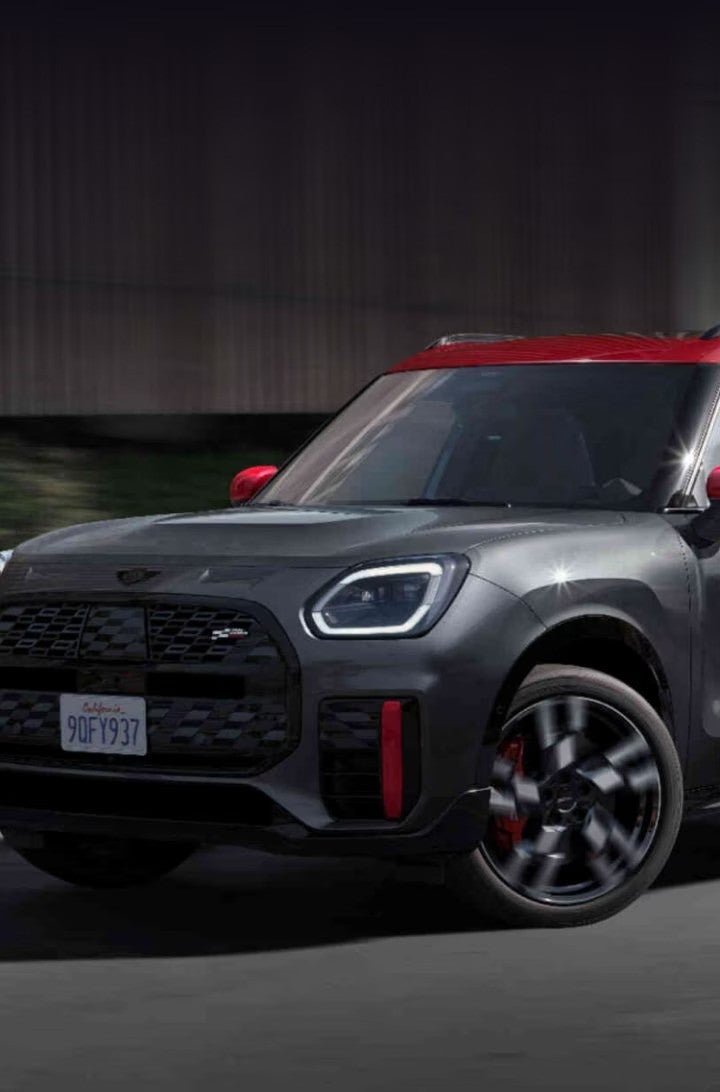  Three-quarters front view of a MINI JCW Countryman ALL4 driving in an urban setting with its shadow underneath it and surroundings blurred out.