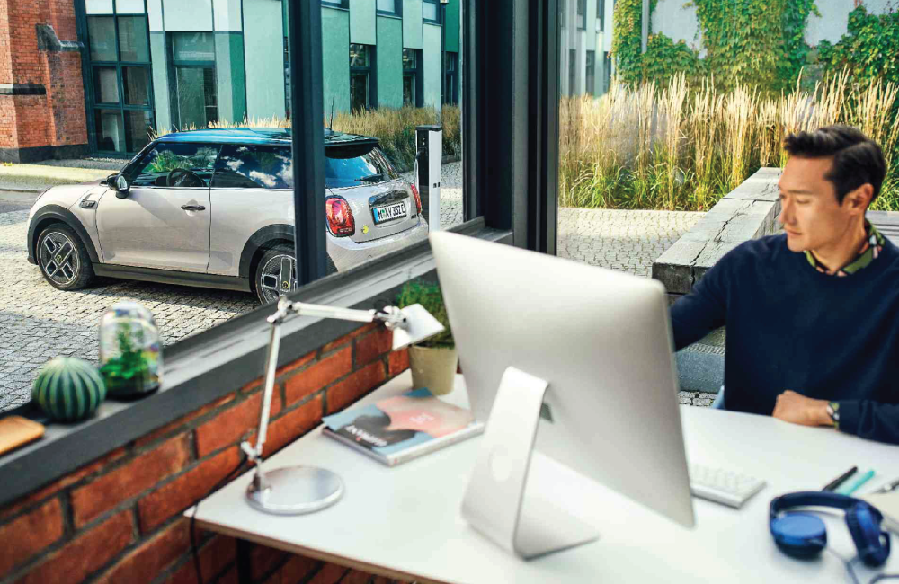 Man sitting at desk on the computer with a MINI parked on the street outside behind him